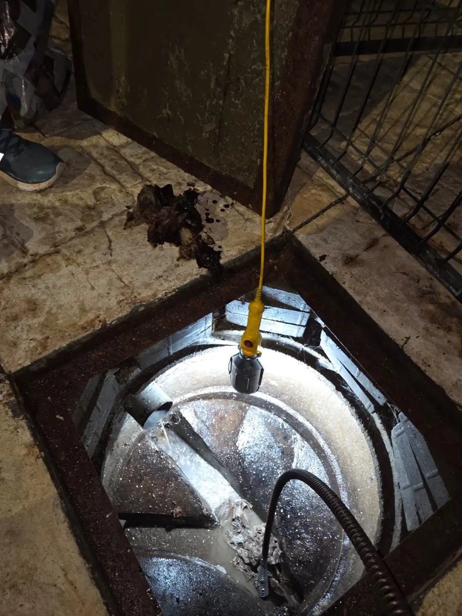 Inspección con foco y sonda dentro de una cámara de alcantarillado de noche — trabajo real